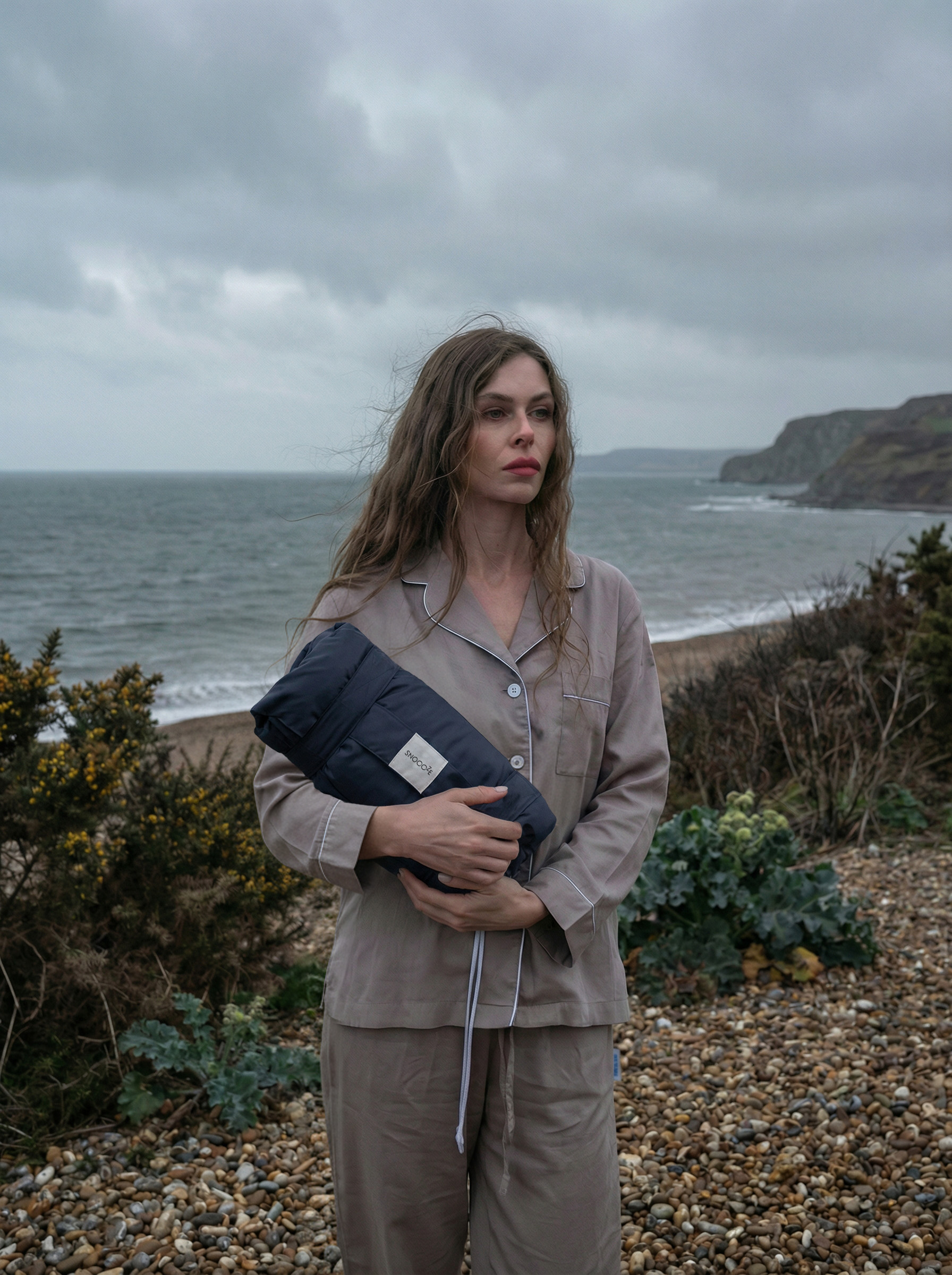A person holding a packed Snoooze travel pillow near the coast.